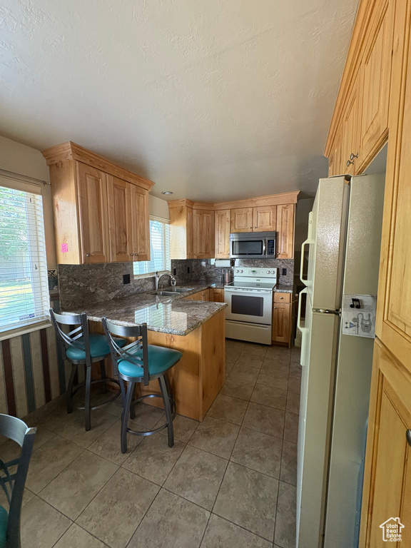 Kitchen with white appliances, backsplash, a sink, a peninsula, and light tile patterned floors