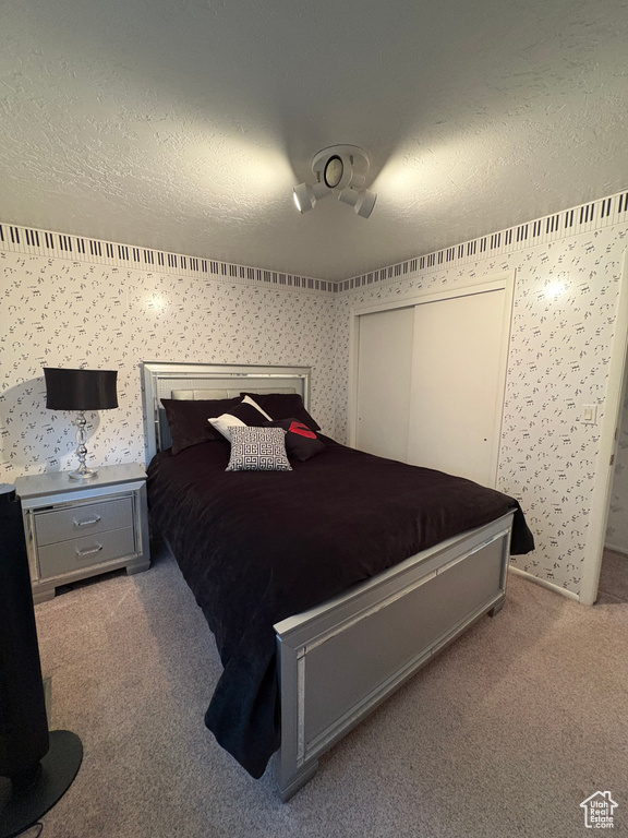 Carpeted bedroom featuring a textured ceiling, wallpapered walls, and a closet