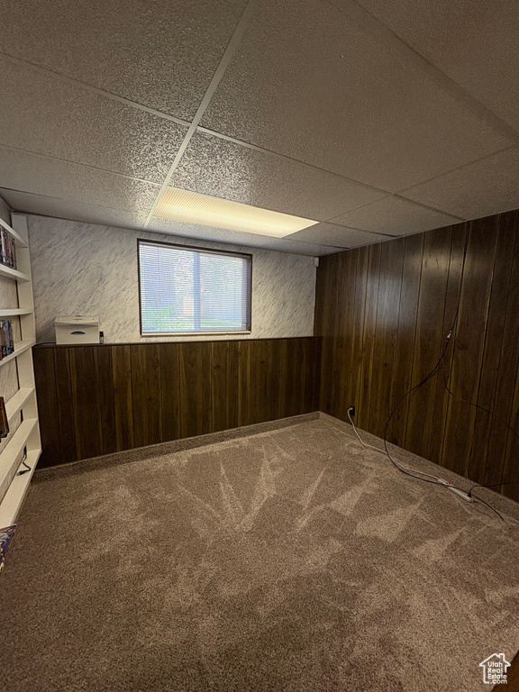 Carpeted spare room with wood walls and a paneled ceiling
