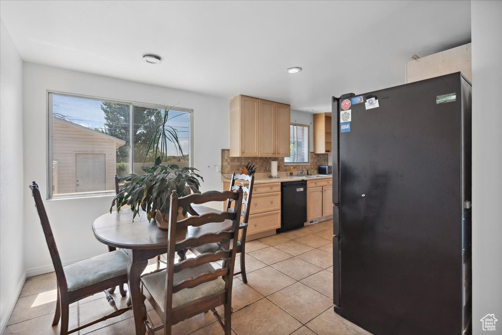 Kitchen featuring freestanding refrigerator, black dishwasher, light brown cabinets, light countertops, and healthy amount of natural light