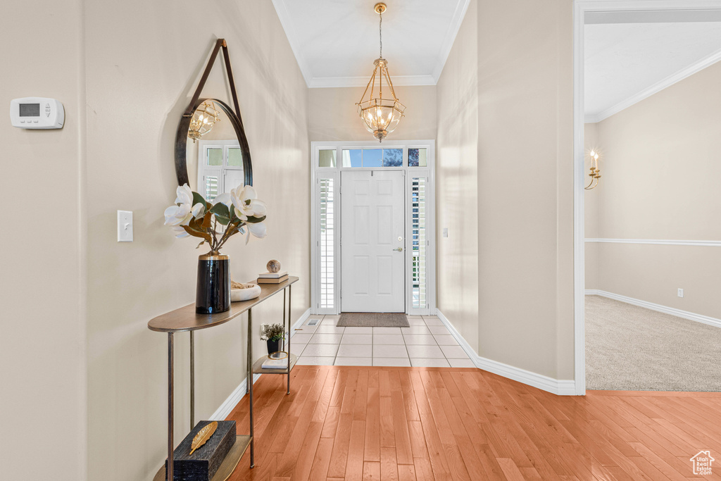 Foyer entrance with a chandelier, crown molding, light wood-type flooring, and baseboards