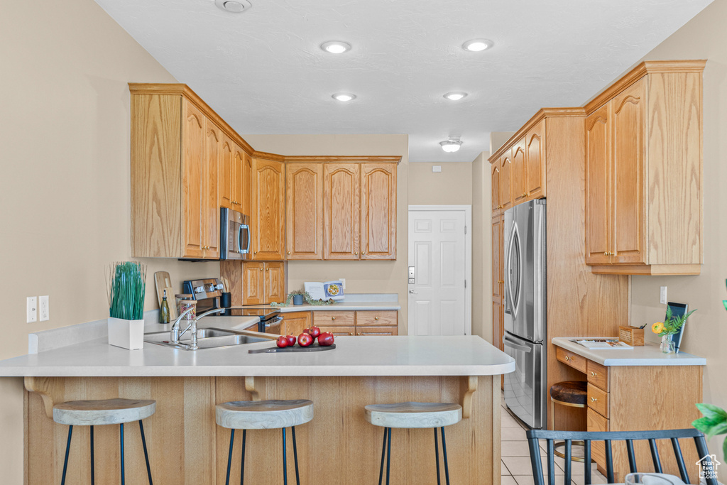 Kitchen with appliances with stainless steel finishes, a peninsula, a kitchen bar, light countertops, and light brown cabinets