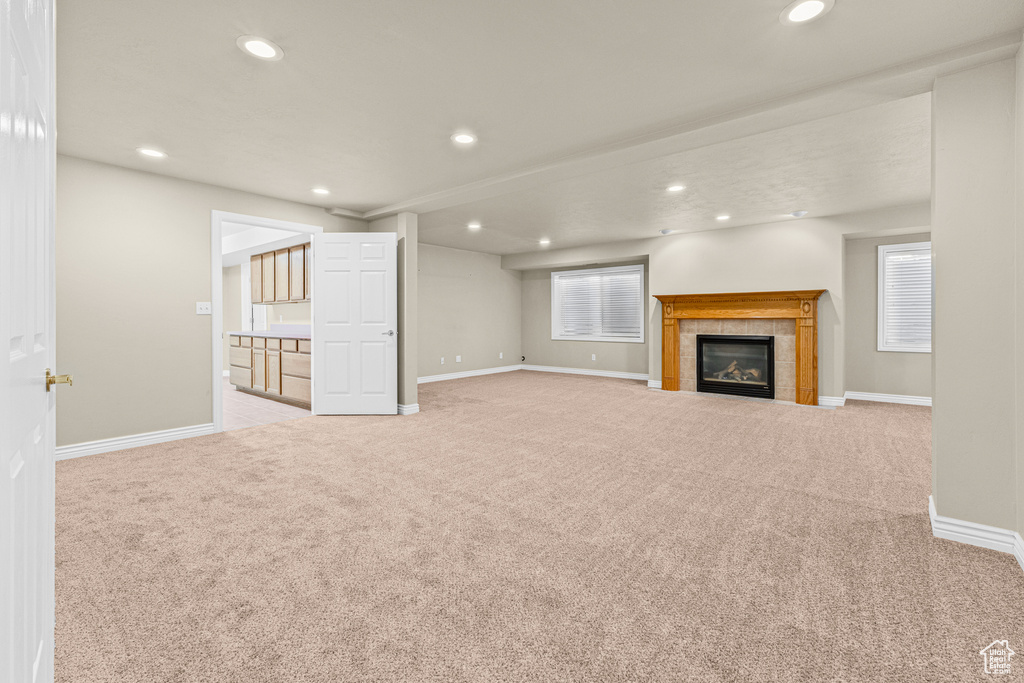 Unfurnished living room with carpet floors, recessed lighting, baseboards, a tile fireplace, and healthy amount of natural light