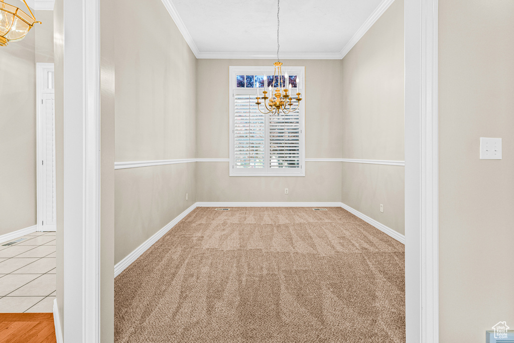 Carpeted empty room with a chandelier, crown molding, and baseboards