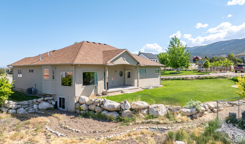 Rear view of property with stucco siding, cooling unit, a yard, a mountain view, and a patio area