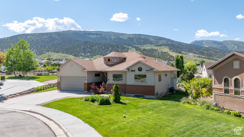 View of front facade featuring a mountain view, driveway, a front yard, a garage, and roof with shingles