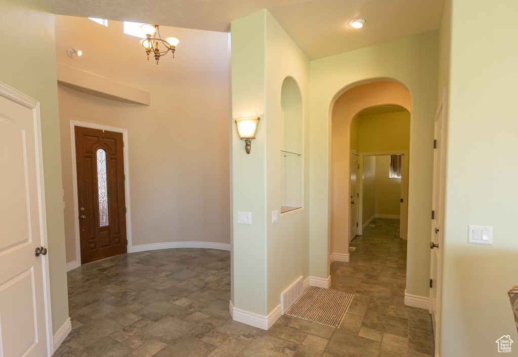 Foyer with stone finish floors, arched walkways, a chandelier, and baseboards