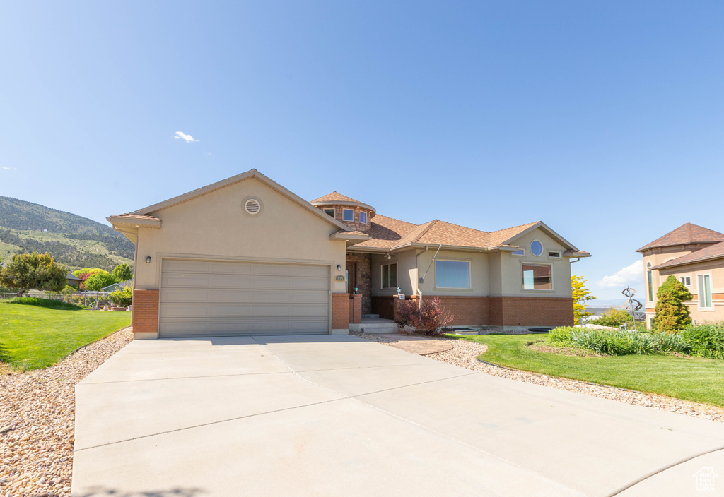 Mediterranean / spanish house with brick siding, an attached garage, driveway, and a front lawn