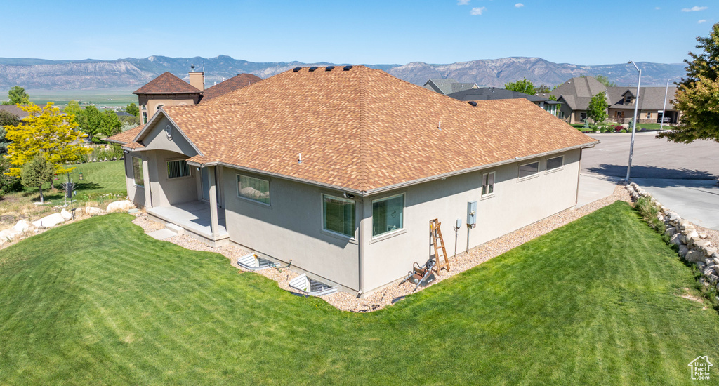 Rear view of house with stucco siding, roof with shingles, and a yard