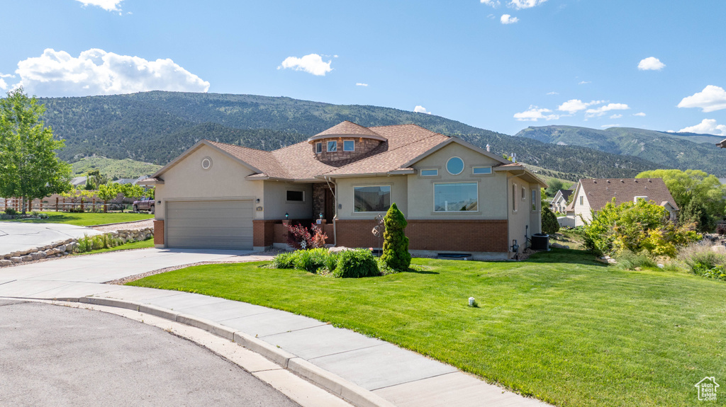 View of front of house featuring a mountain view, a front yard, an attached garage, stucco siding, and driveway