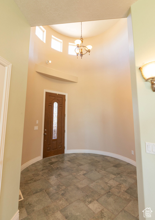Foyer entrance with stone finish floors, a high ceiling, baseboards, and a chandelier