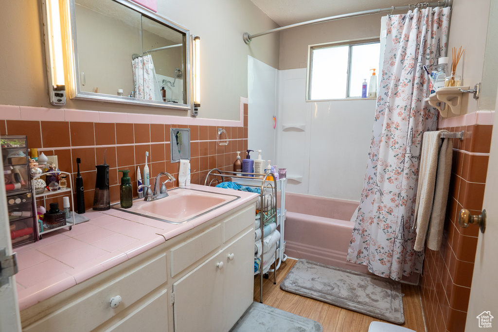 Full bathroom featuring wood finished floors, vanity, shower / bath combo, wainscoting, and tile walls