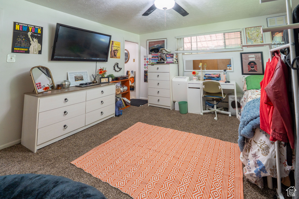 Carpeted bedroom with a textured ceiling, a ceiling fan, and a desk