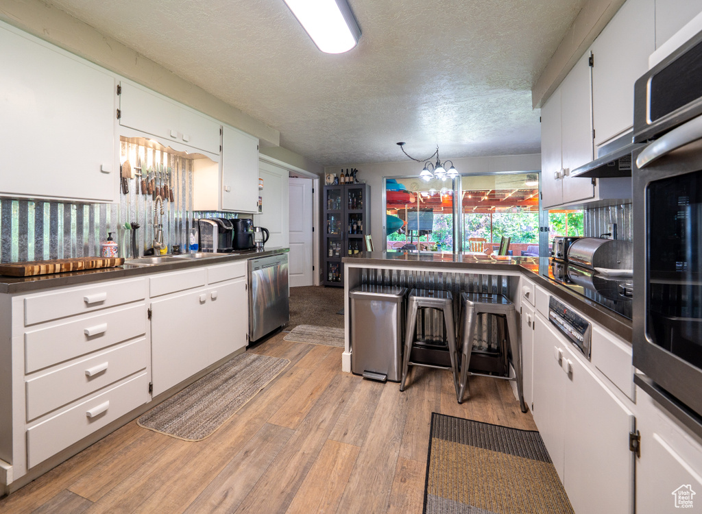 Kitchen featuring appliances with stainless steel finishes, a sink, dark countertops, light wood finished floors, and a textured ceiling