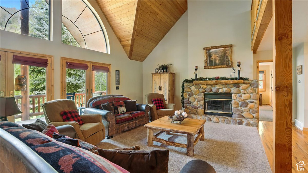Carpeted living area featuring high vaulted ceiling, wood ceiling with exposed beams, a stone fireplace, and wood finished floors