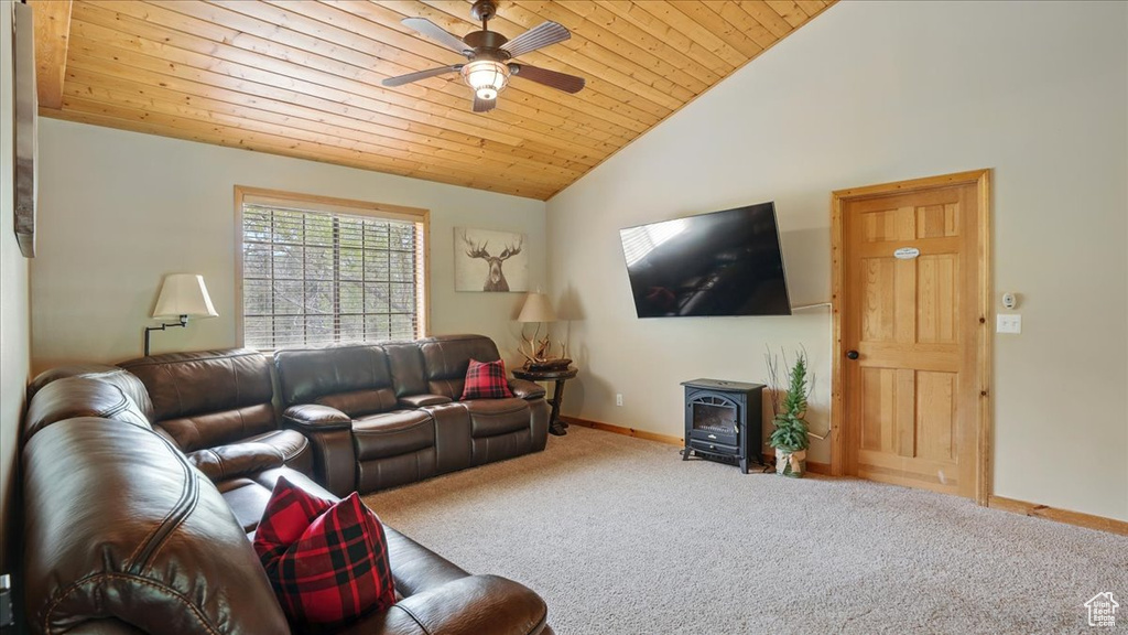 Living room with a wood stove, lofted ceiling, carpet flooring, ceiling fan, and baseboards