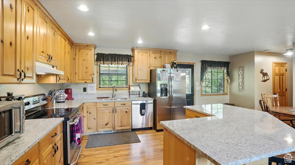 Kitchen featuring stainless steel appliances, under cabinet range hood, a sink, a kitchen island, and light wood-style flooring