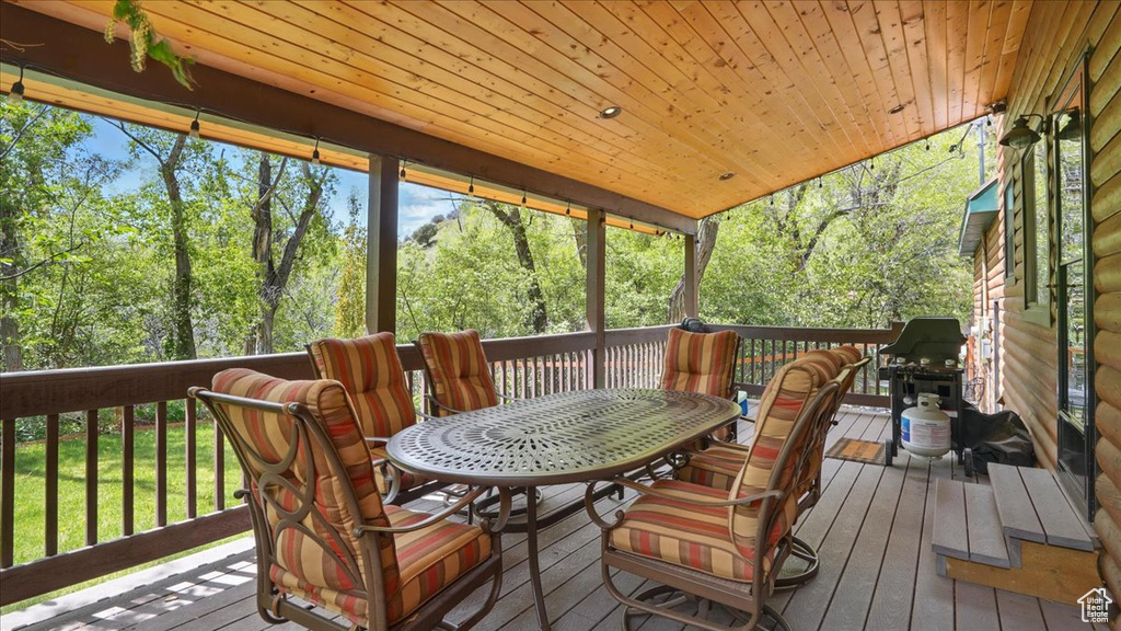 Wooden terrace featuring outdoor dining area, grilling area, and view of scattered trees
