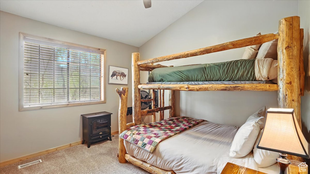 Carpeted bedroom featuring a wood stove, lofted ceiling, ceiling fan, and baseboards