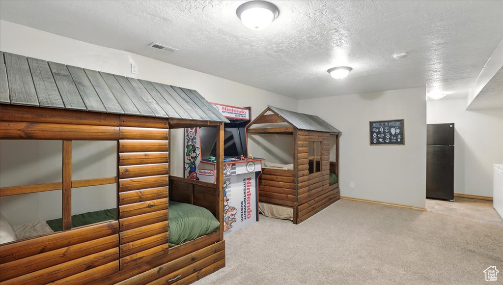 Carpeted bedroom with freestanding refrigerator, a textured ceiling, and baseboards