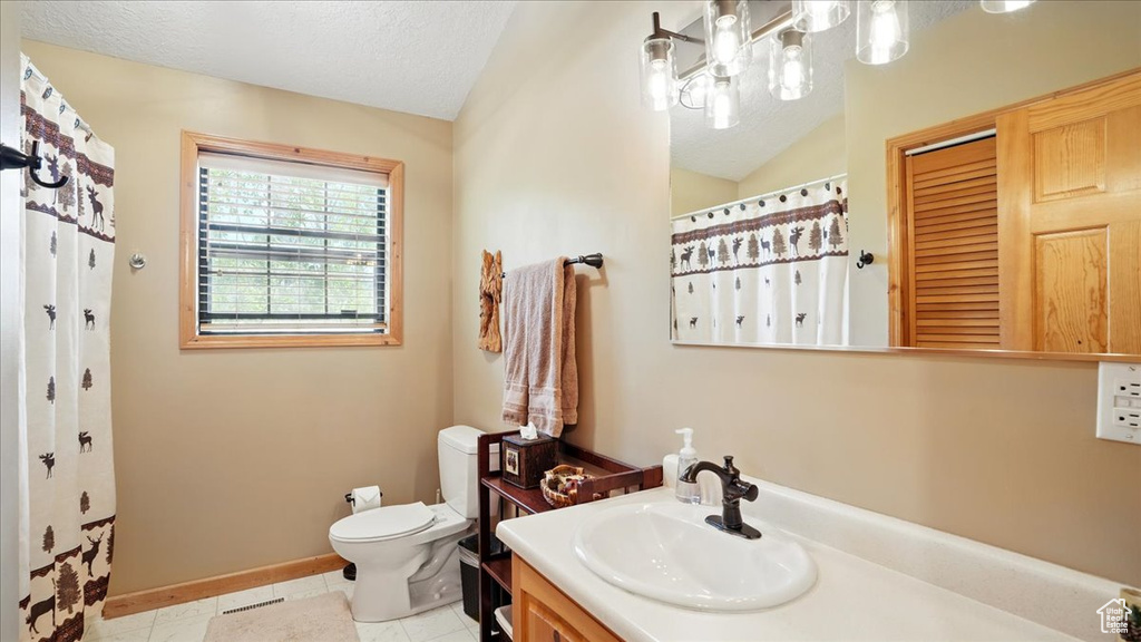 Full bath featuring vanity, toilet, a textured ceiling, baseboards, and vaulted ceiling