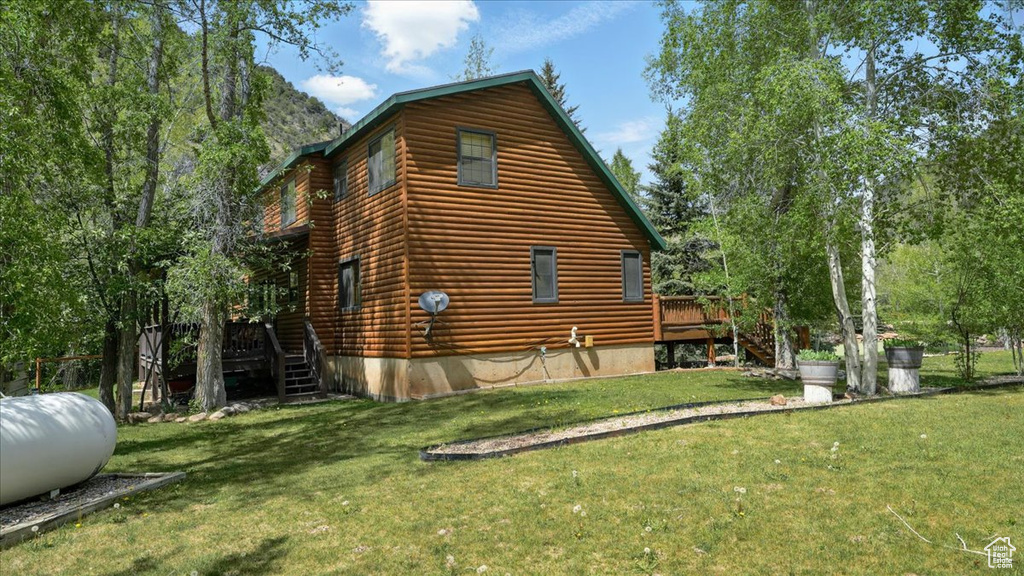 View of side of property featuring stairs, a wooden deck, and a lawn