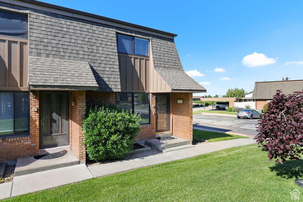 View of front facade featuring brick siding, entry steps, a front lawn, and roof with shingles