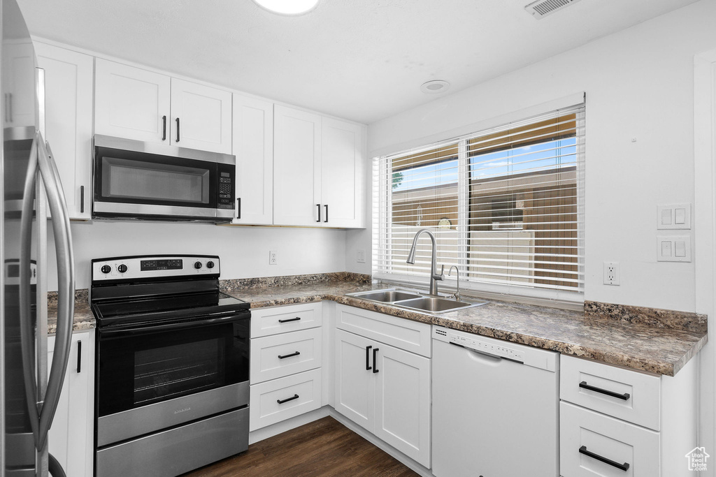 Kitchen featuring appliances with stainless steel finishes, a sink, white cabinets, and dark wood-type flooring