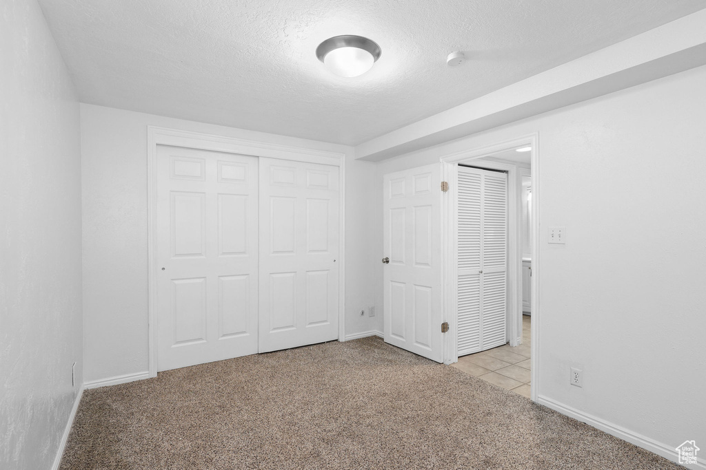 Unfurnished bedroom featuring light colored carpet, a textured ceiling, baseboards, and a closet