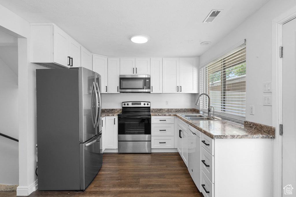 Kitchen featuring stainless steel appliances, a sink, white cabinetry, and dark wood-style flooring