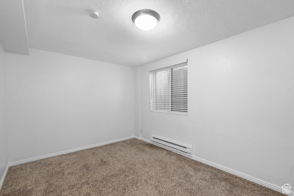Empty room with baseboard heating, carpet floors, baseboards, a smoke detector, and a textured ceiling