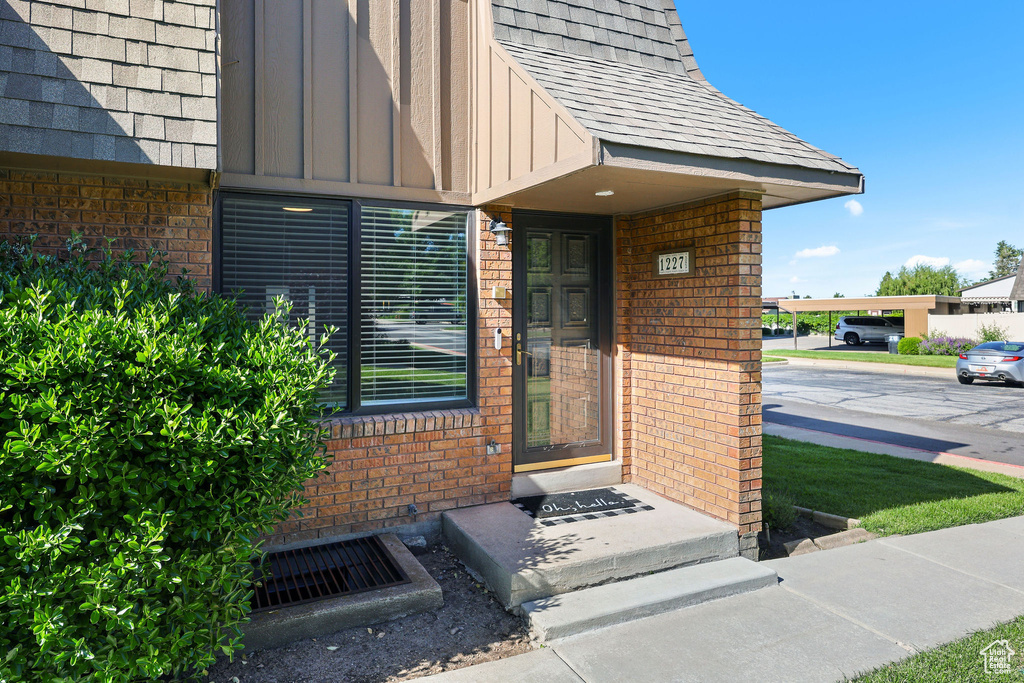 View of exterior entry featuring brick siding, roof with shingles, and board and batten siding