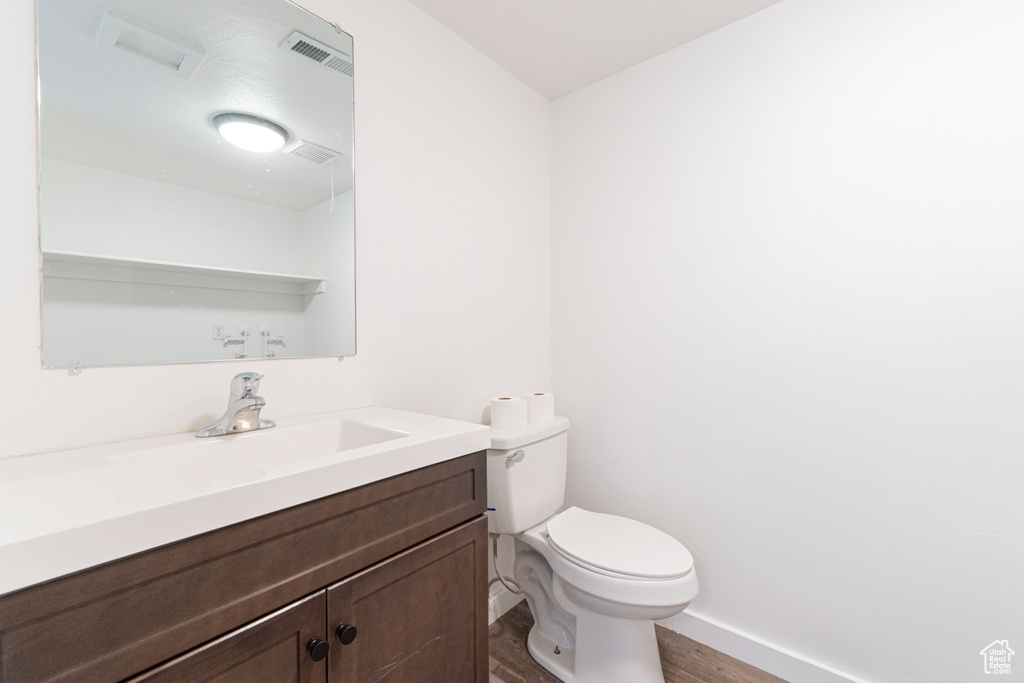 Half bath featuring wood finished floors, vanity, toilet, and baseboards