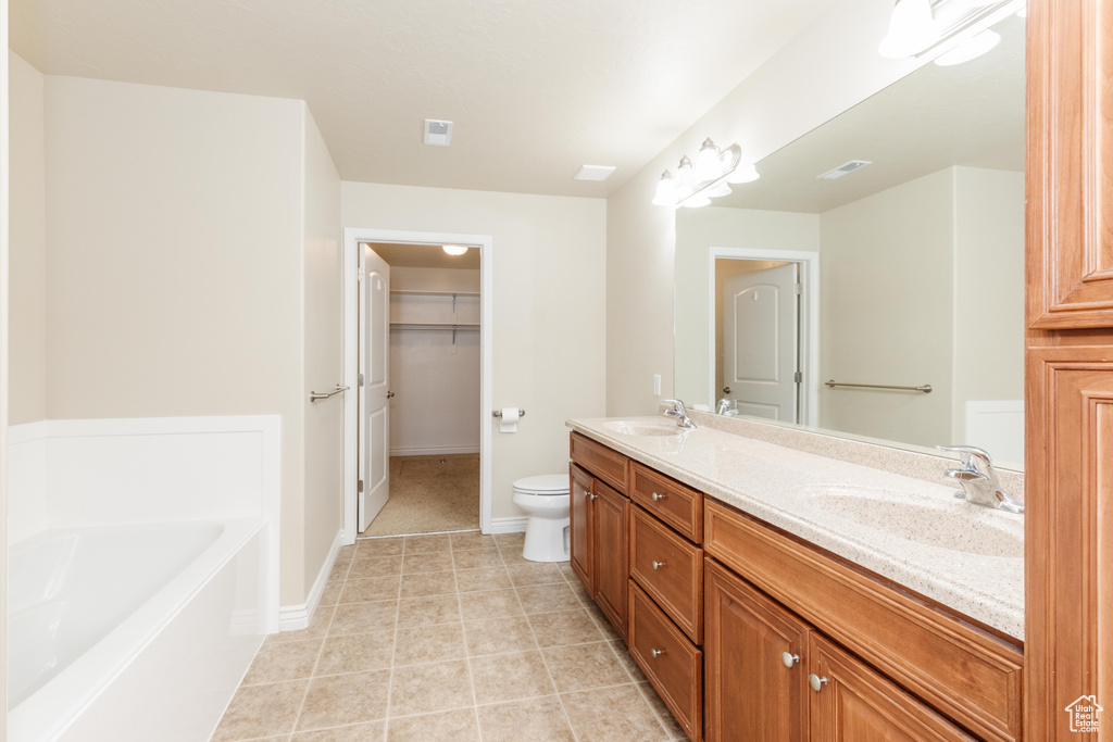 Full bath with double vanity, a bath, toilet, tile patterned floors, and a walk in closet