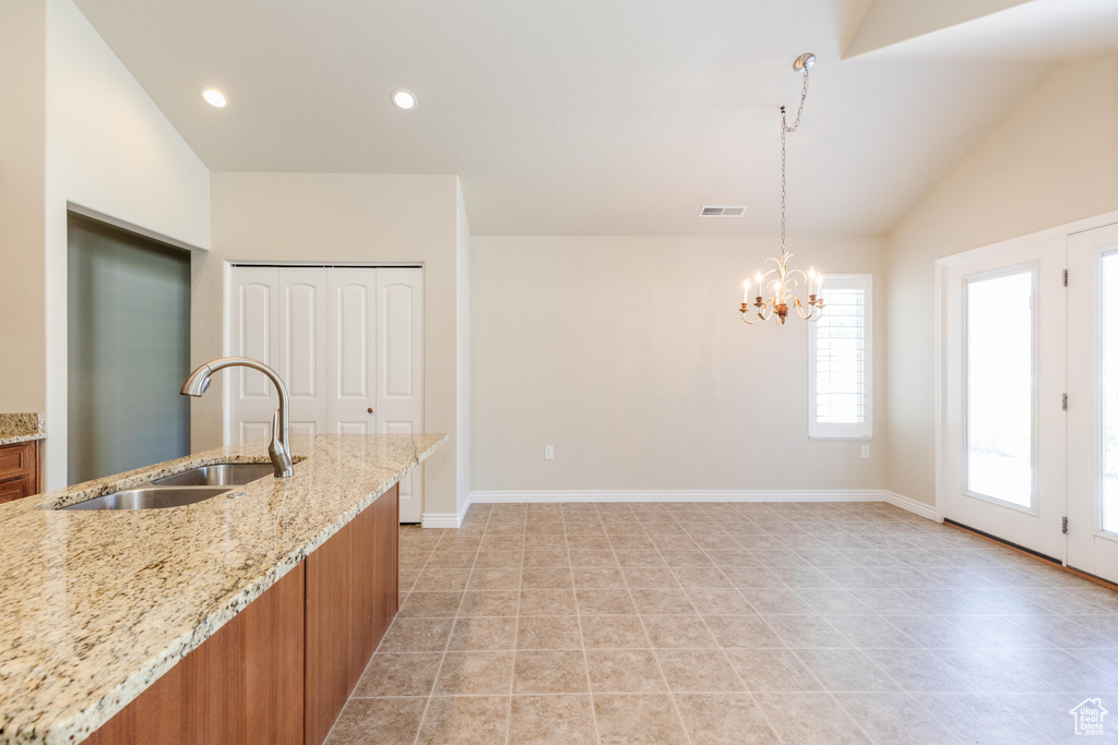 Kitchen featuring a sink, brown cabinets, lofted ceiling, baseboards, and a chandelier