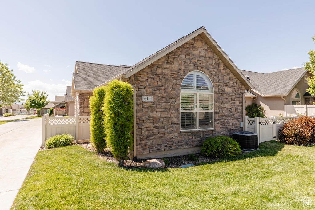 View of home's exterior with stone siding, central AC, roof with shingles, and a gate