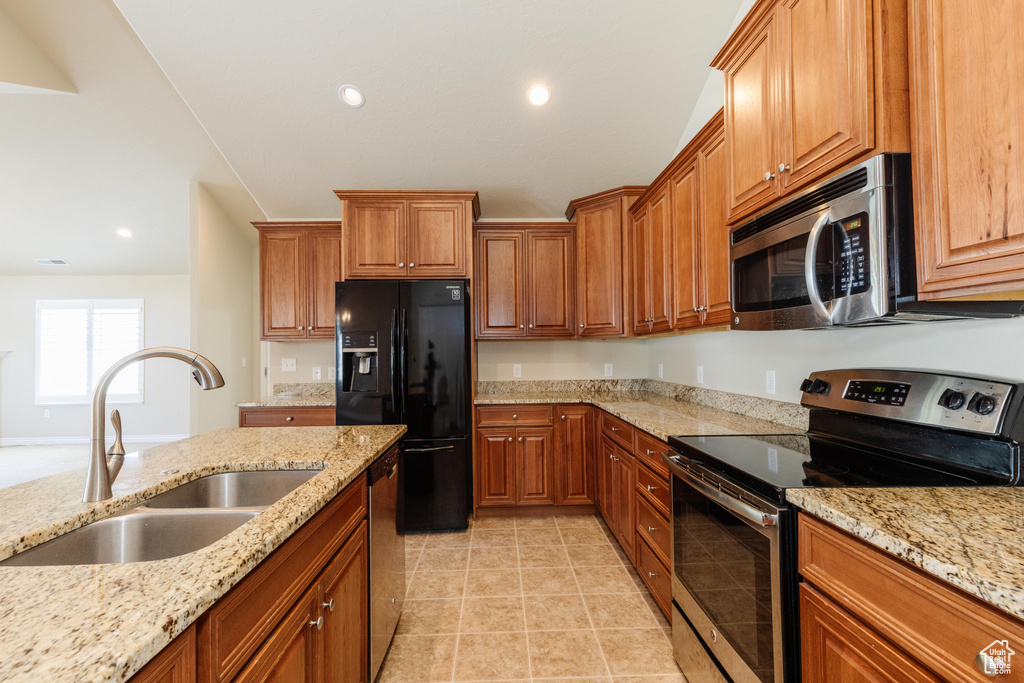 Kitchen featuring appliances with stainless steel finishes, a sink, brown cabinetry, recessed lighting, and light stone counters