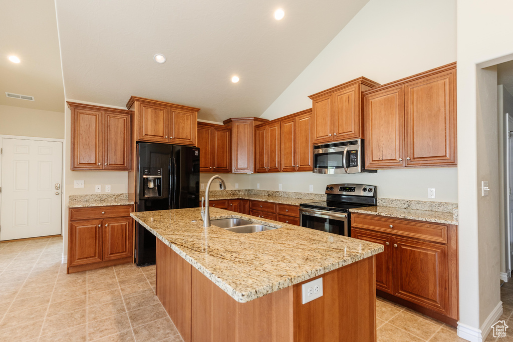 Kitchen featuring appliances with stainless steel finishes, a sink, vaulted ceiling, brown cabinetry, and an island with sink