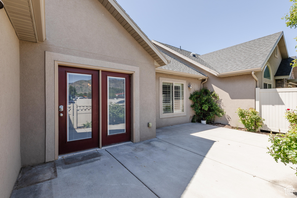 Property entrance featuring stucco siding, a patio area, and a shingled roof