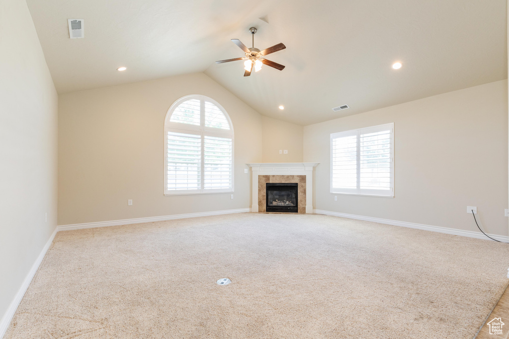 Unfurnished living room with a ceiling fan, vaulted ceiling, a fireplace, light colored carpet, and baseboards