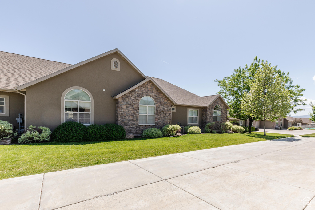 View of front of home with stucco siding, a front yard, stone siding, and roof with shingles
