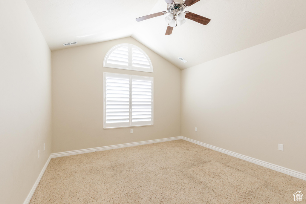 Carpeted empty room with lofted ceiling, a ceiling fan, and baseboards