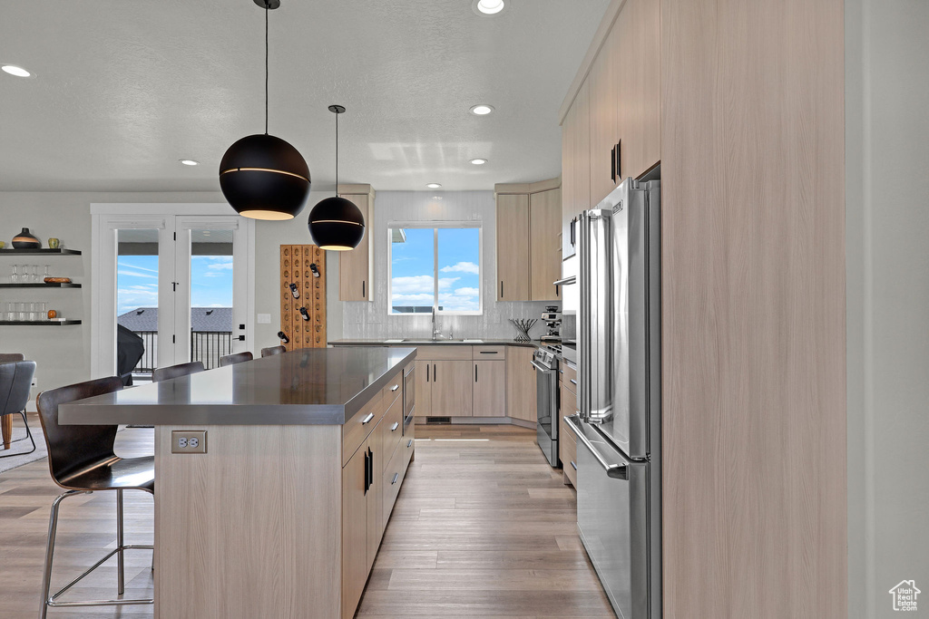 Kitchen featuring light brown cabinets, stainless steel appliances, a sink, modern cabinets, and a kitchen breakfast bar