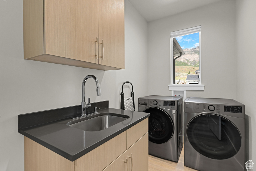 Laundry area featuring washing machine and dryer, cabinet space, and light wood-type flooring