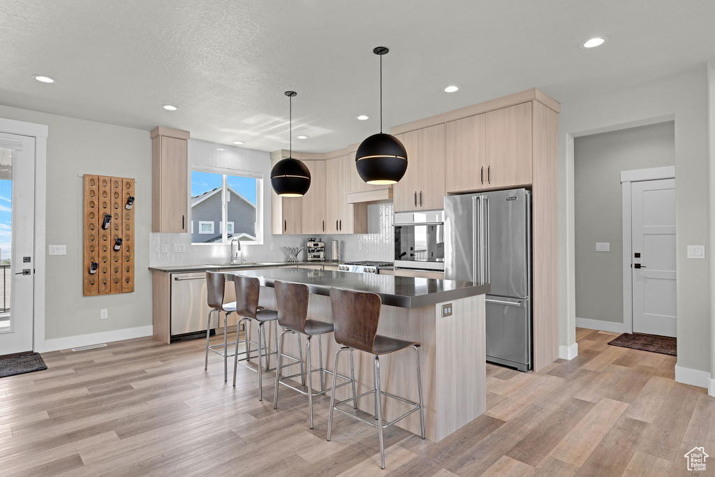 Kitchen featuring stainless steel appliances, a center island, a kitchen bar, light wood-style floors, and tasteful backsplash