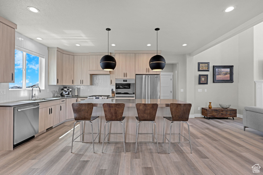 Kitchen featuring appliances with stainless steel finishes, light wood-style floors, a sink, a center island, and light brown cabinetry