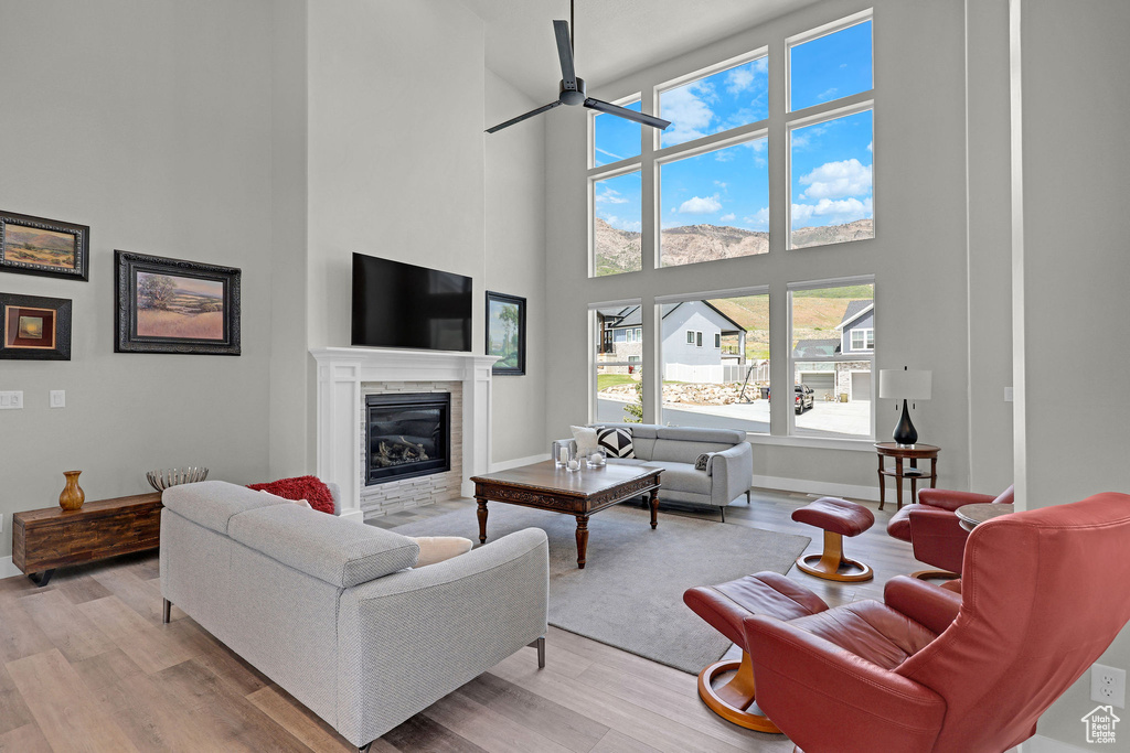 Living area with a towering ceiling, ceiling fan, a glass covered fireplace, light wood finished floors, and baseboards