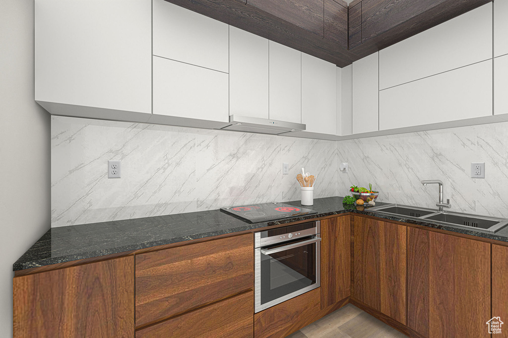 Kitchen with oven, a sink, black electric stovetop, and tasteful backsplash