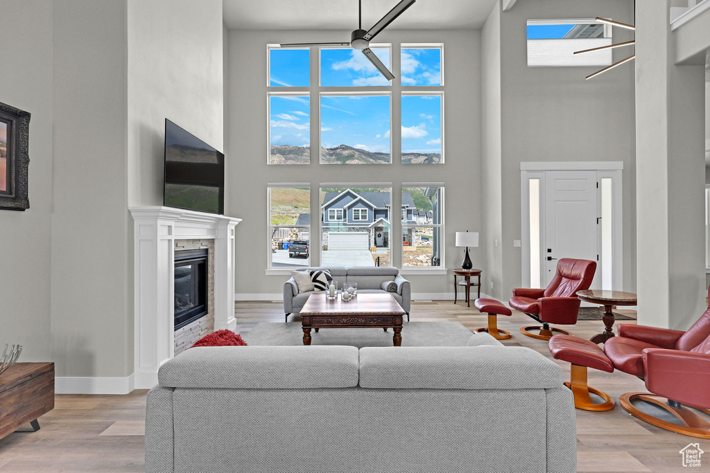 Living room featuring a towering ceiling, a glass covered fireplace, light wood-type flooring, and baseboards