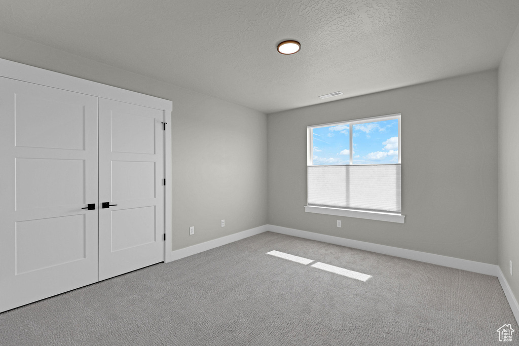 Unfurnished bedroom with carpet flooring, baseboards, a textured ceiling, and a closet